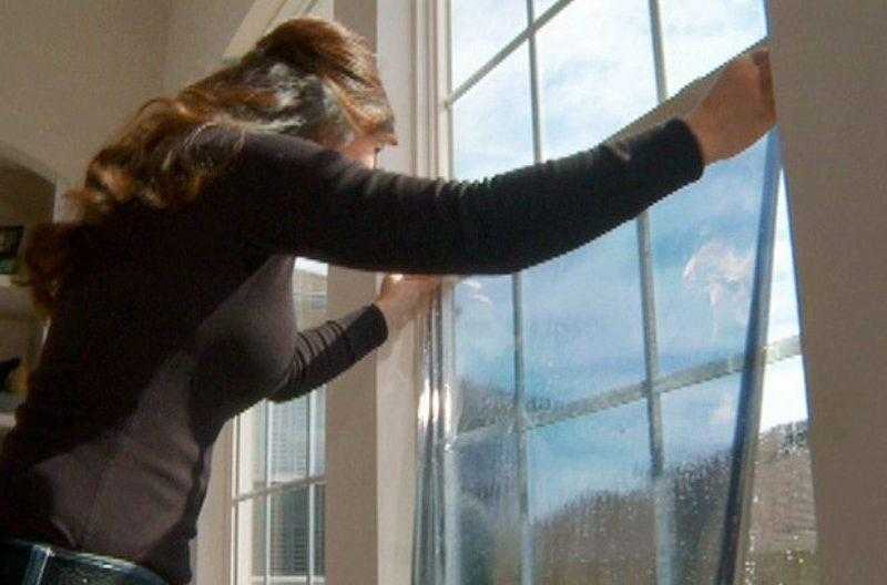 Женщина приклеивает пленочное покрытие на стекло